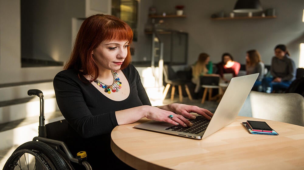 a girl in wheelchair  is sitting at the table with a computer